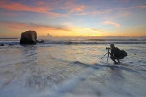 man taking a picture of the ocean on body of water during golden hour