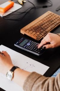 bookkeeper writing down on paper while using calculator